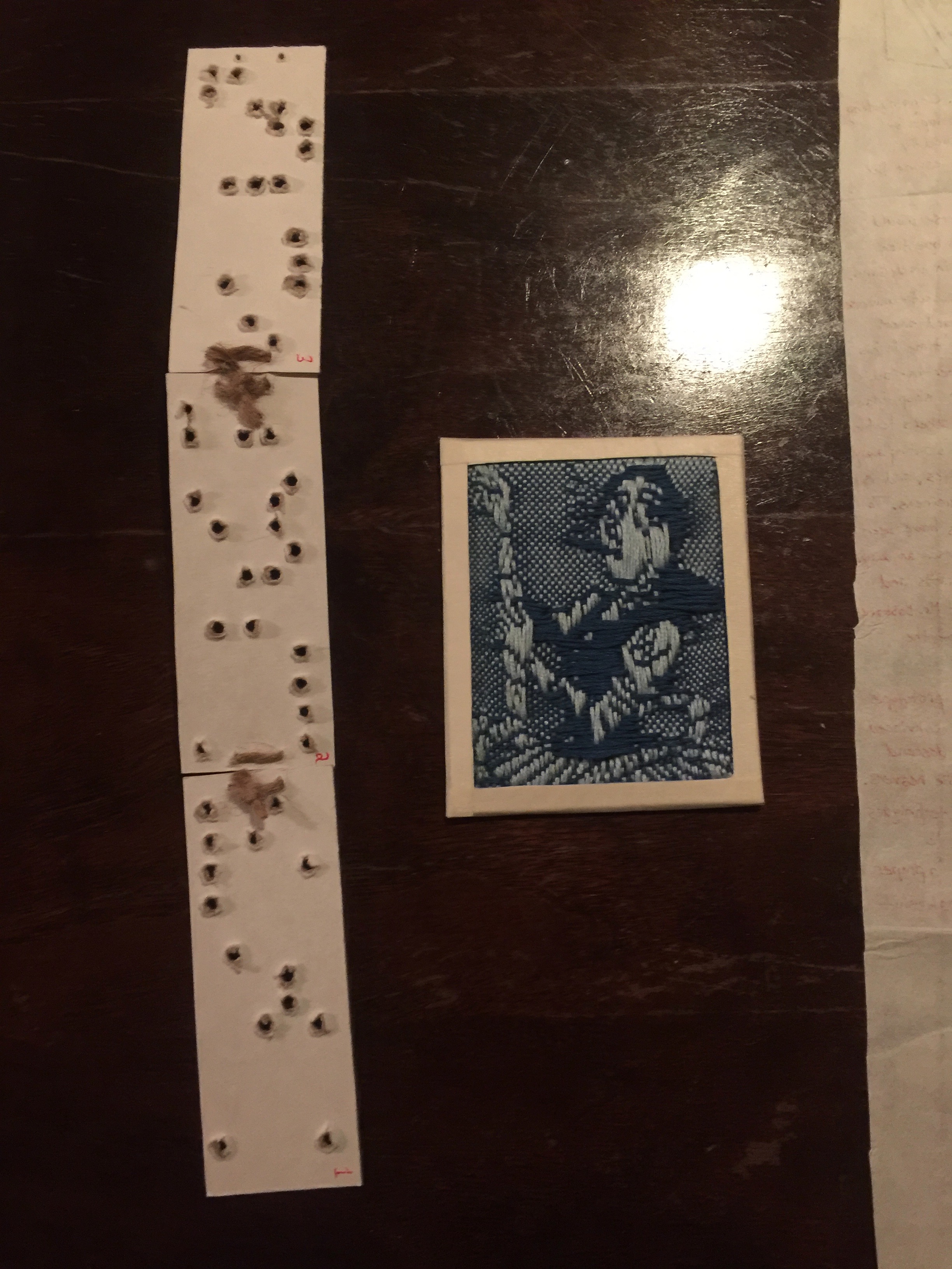 A model Jacquard loom punchcard and a woven figure of Ada Lovelace partly drawn from the pattern encoded in these cards.